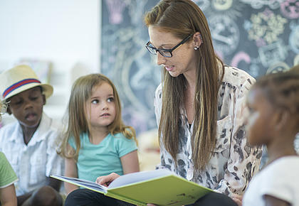 Eine junge Lehrerin liest Kindern aus einem Buch vor.